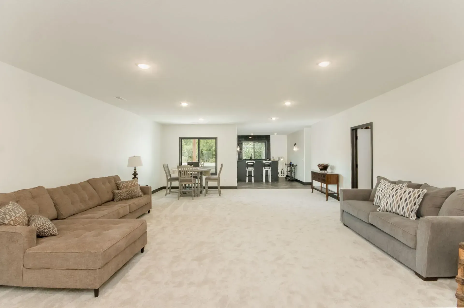 Spacious white living room with beige and gray sofas, carpeted floor, and a dining area in the back