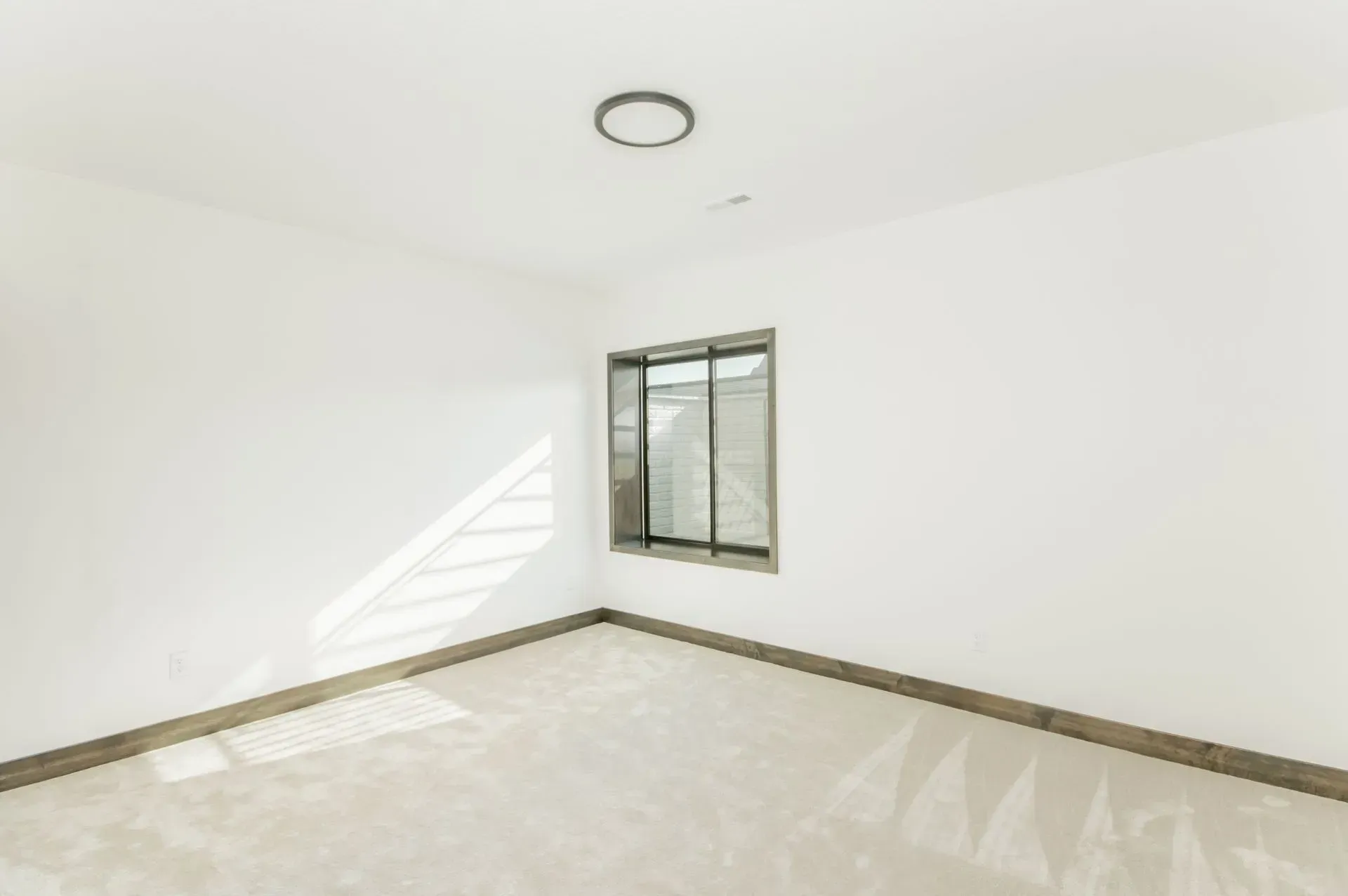 Bright empty room with white walls, tiled floor, and a small window casting sunlight.