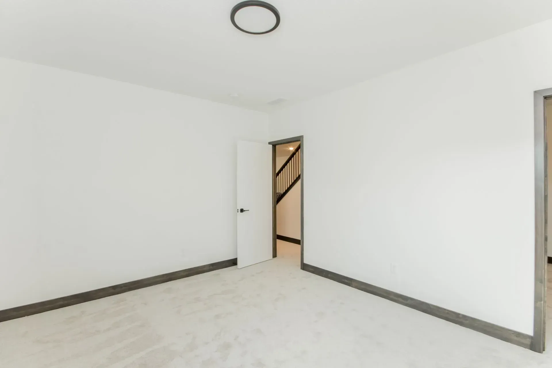 Empty white room with light flooring, dark trim, ceiling light, and an open doorway.
