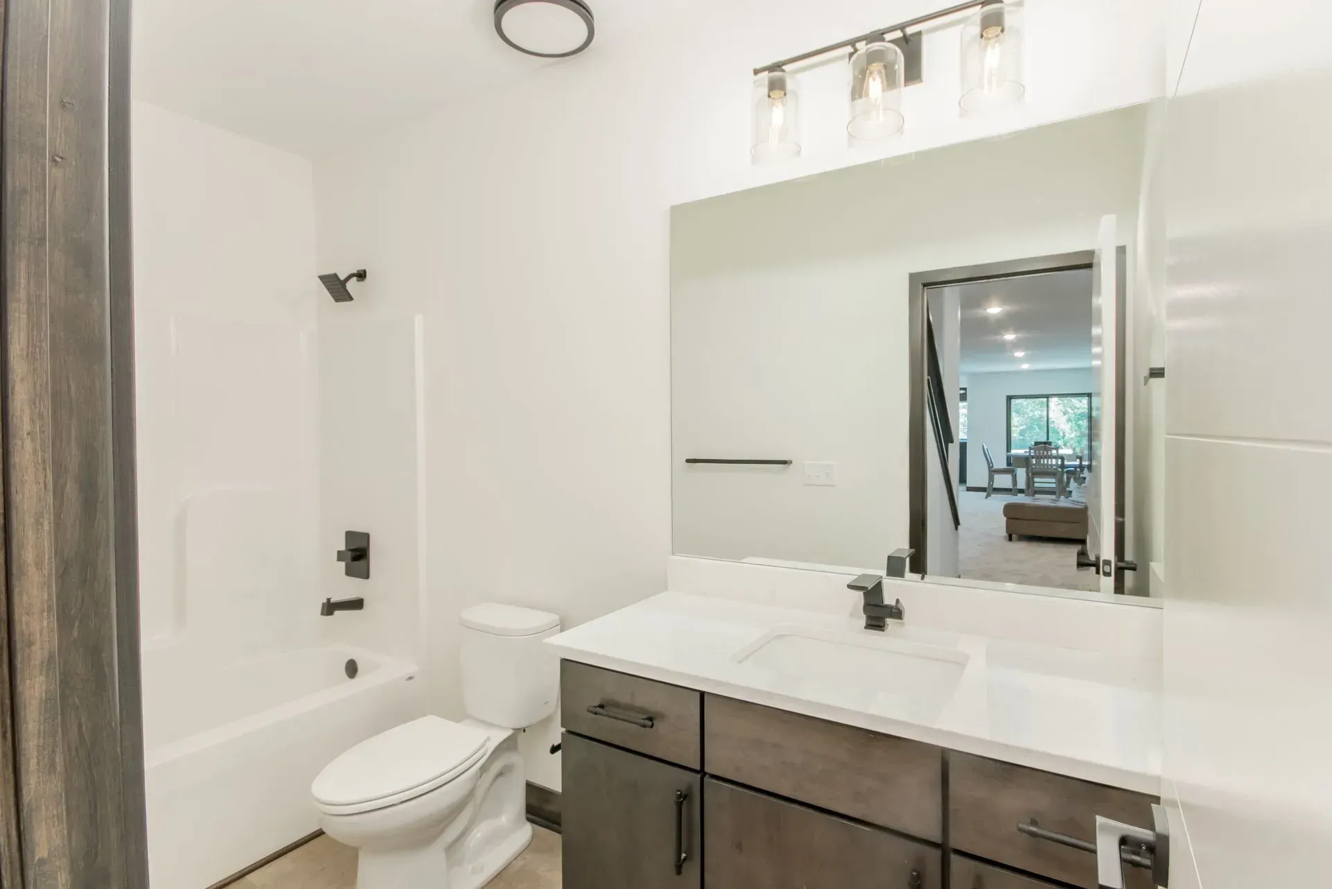 Bright modern bathroom with white walls, toilet, vanity sink, and large mirror