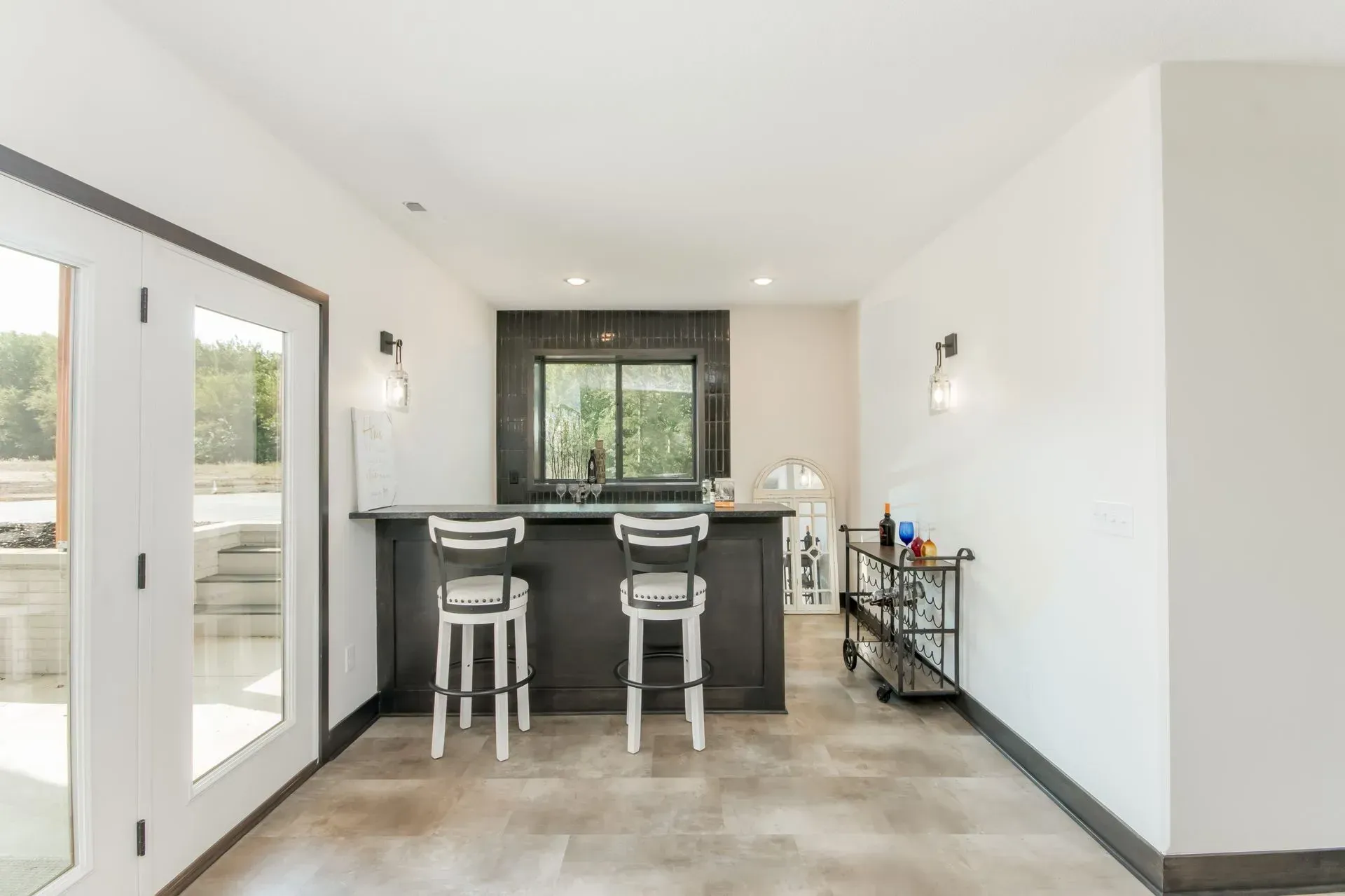 Bright modern kitchen with bar stools, tile floor, white walls, and large glass doors.