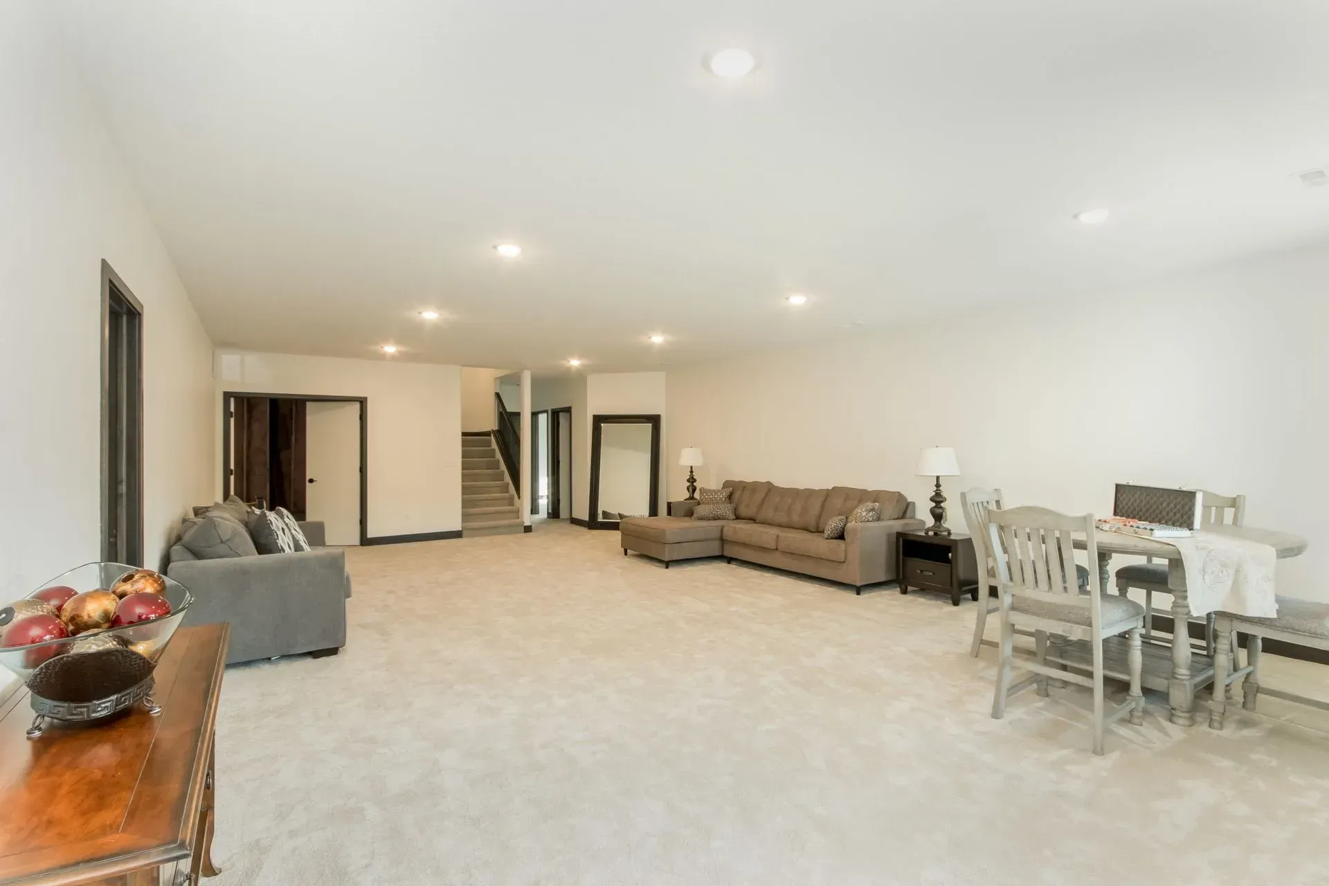 Spacious living room with beige carpet, sofas, dining table, and recessed ceiling lights