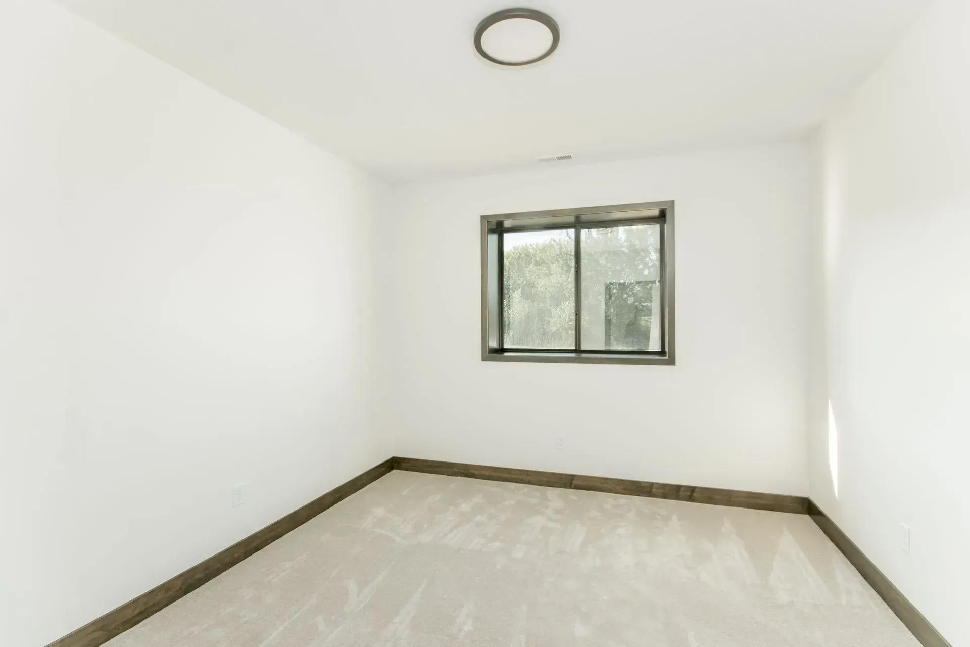 Empty white room with a small window, beige carpet, and dark trim
