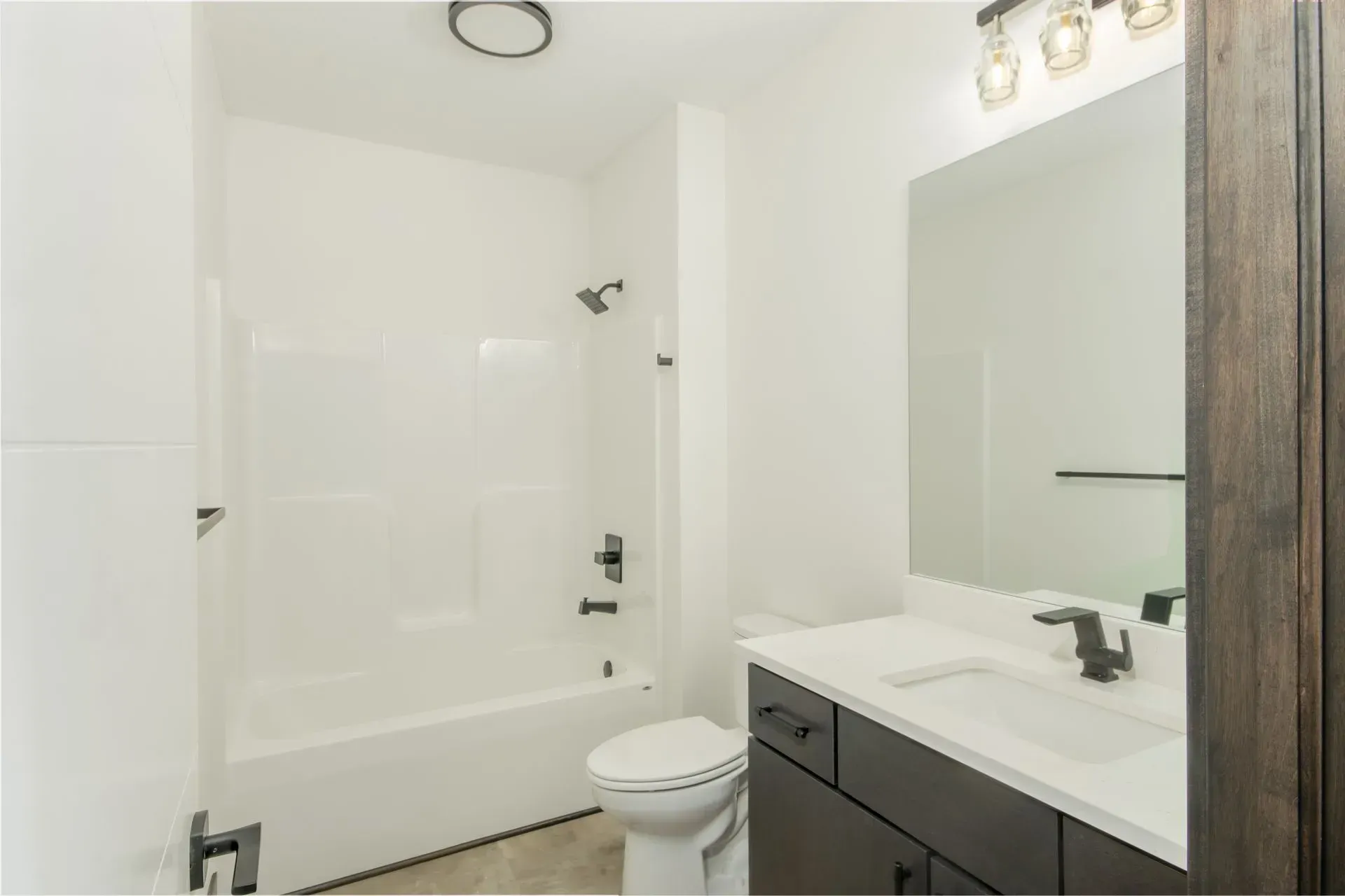White bathroom with a tub, toilet, vanity sink, and large mirror.