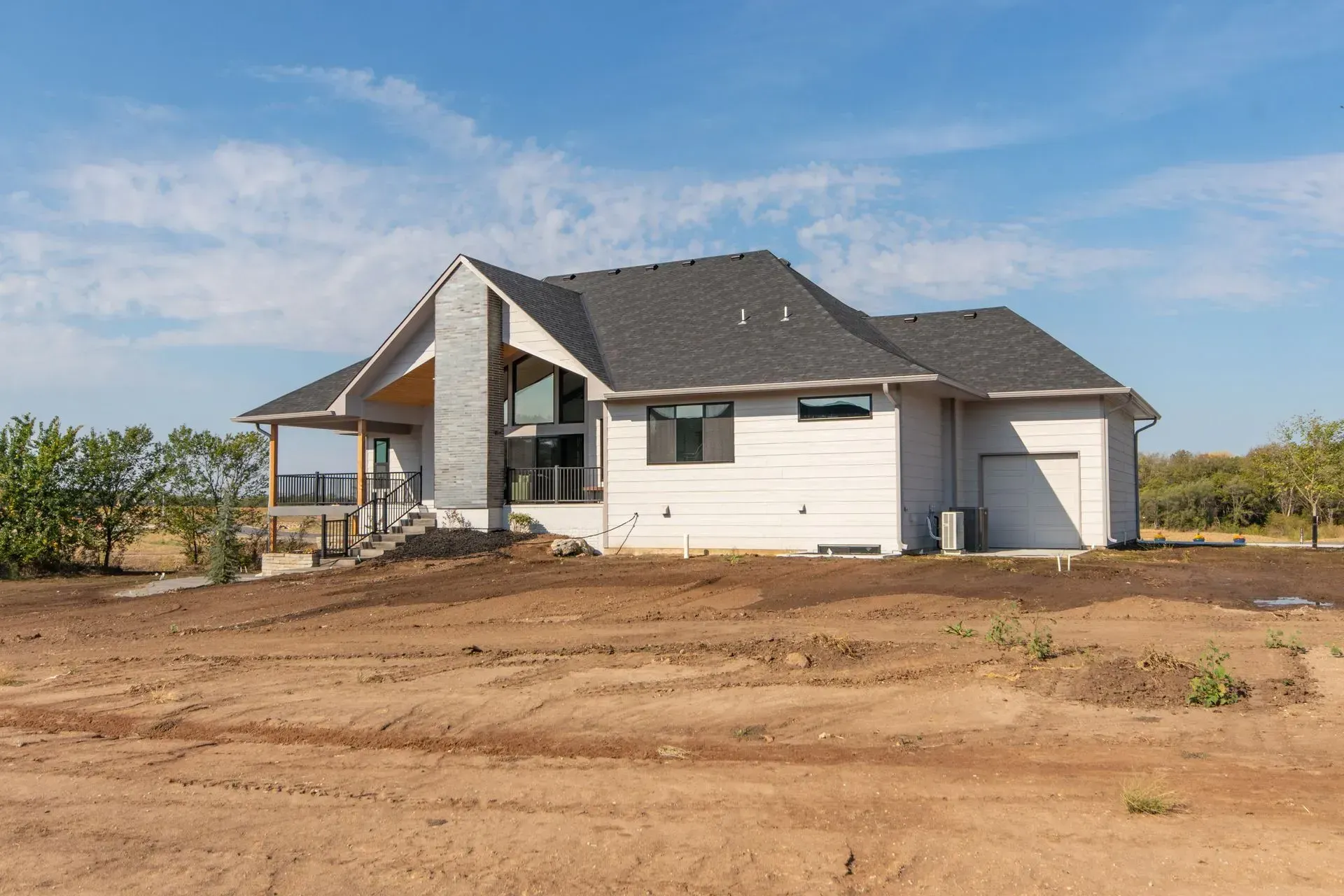 New white house with a porch and garage on a bare dirt lot under a blue sky