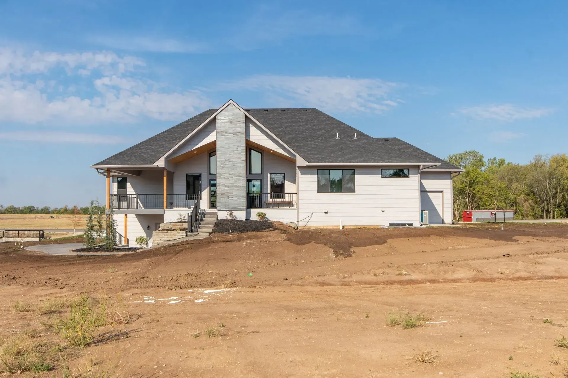 New suburban house with gray roof and white siding on a bare dirt lot under a blue sky