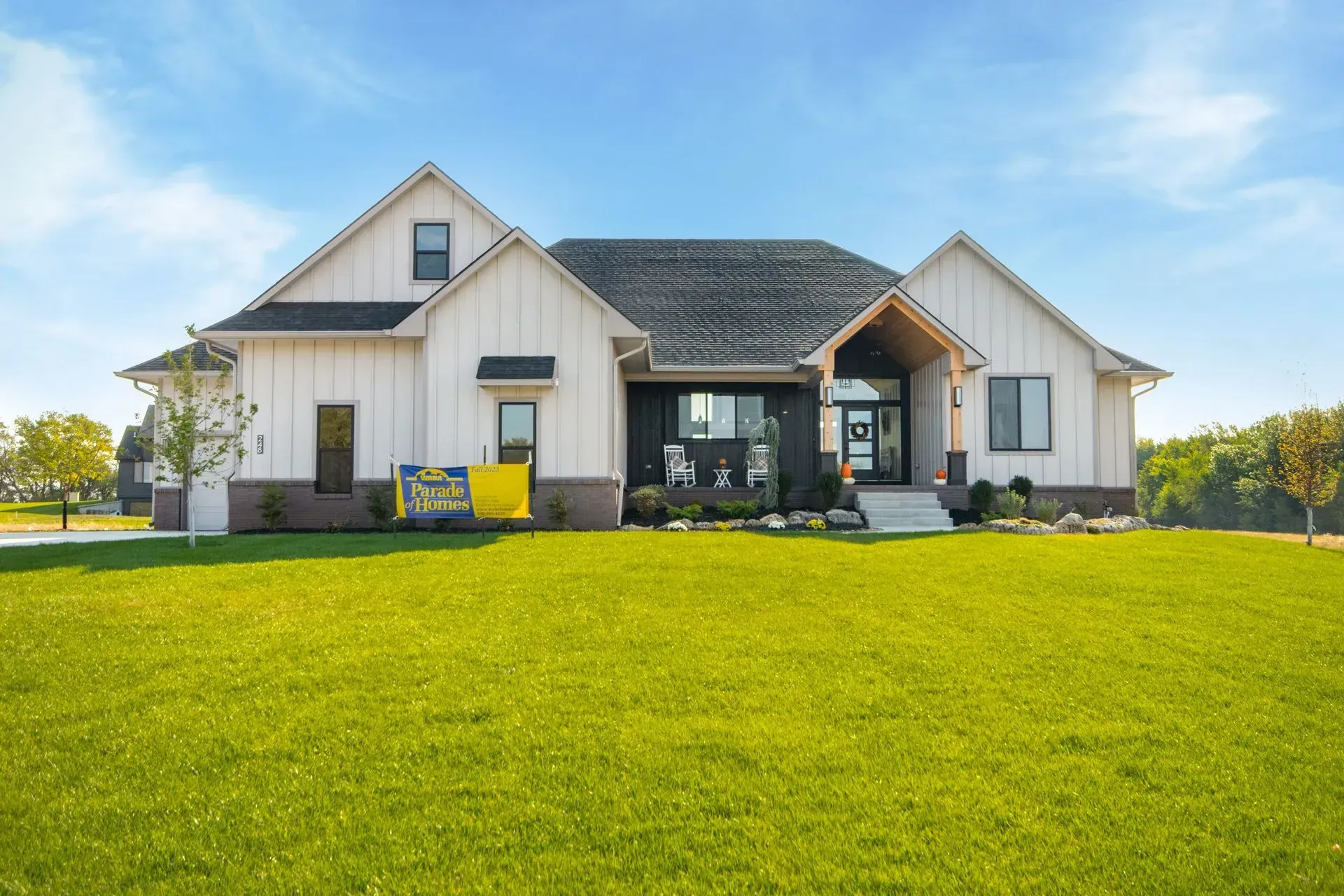 Modern white house with dark roof and large green lawn under a blue sky
