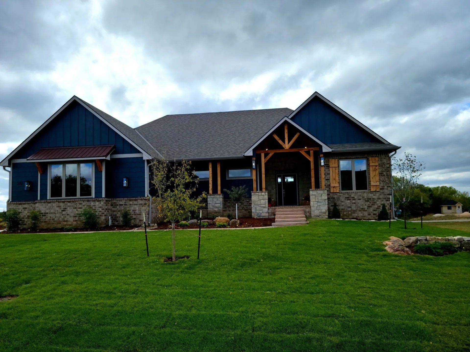 Blue stone house with a gabled roof and large green lawn under a cloudy sky.