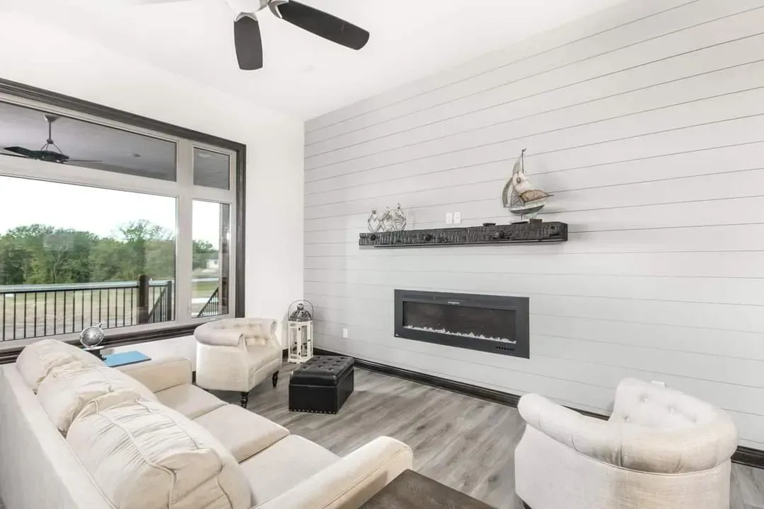 Bright modern living room with white sofa, fireplace, wall shelf, ceiling fan, and large window view