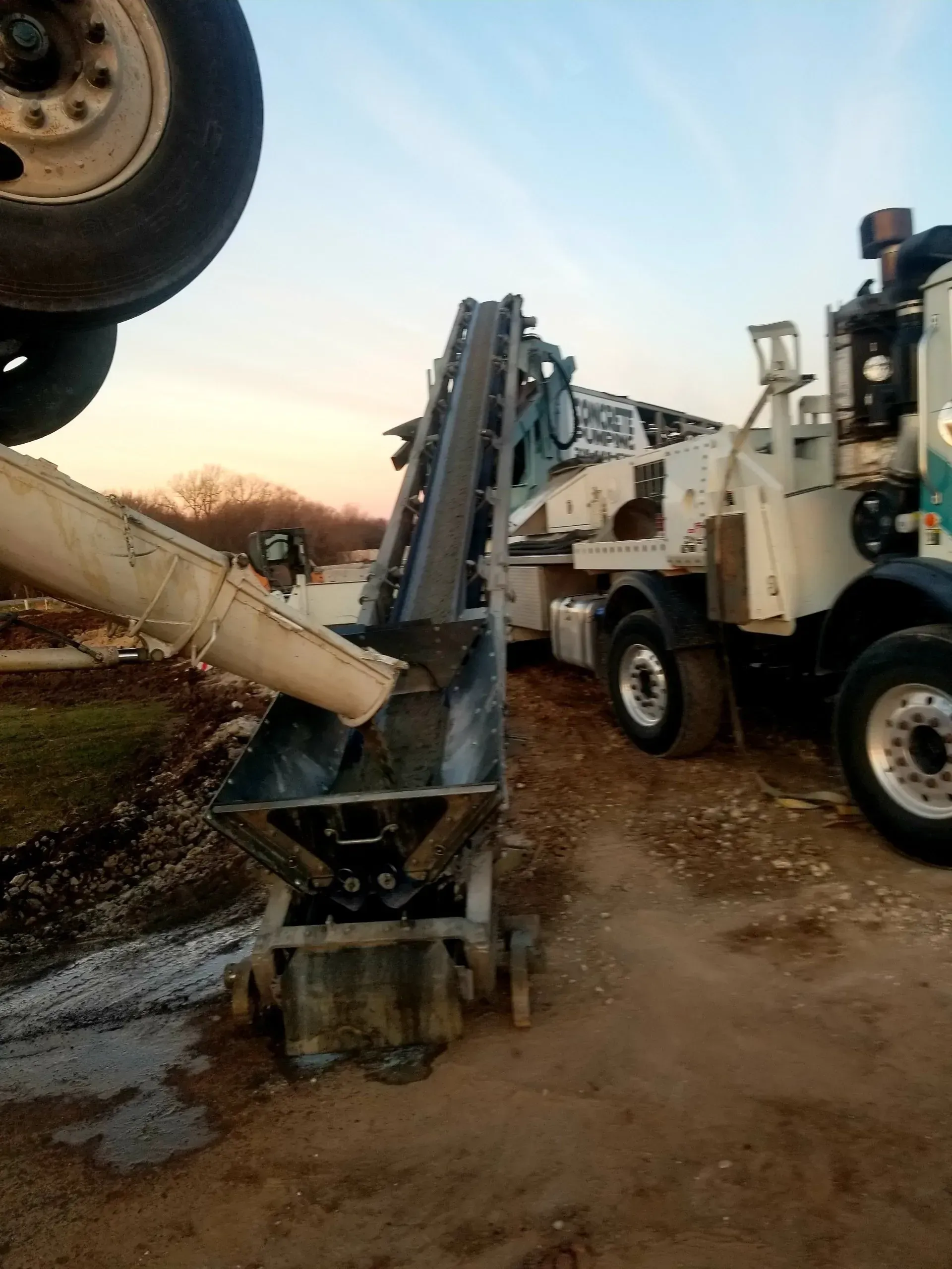 White utility truck with drilling rig and concrete auger on a dirt site at sunset