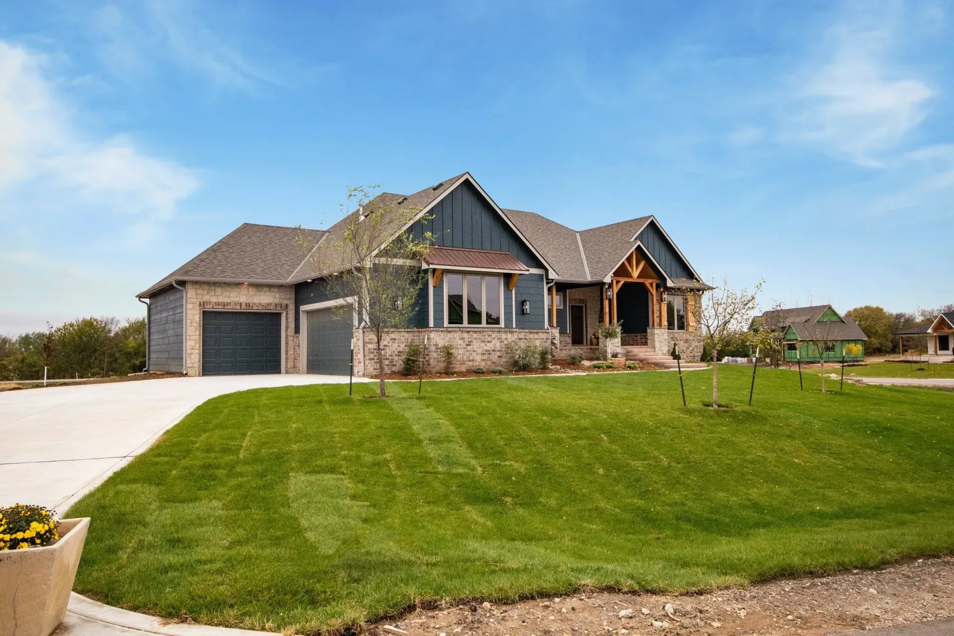 Single-story brick house with three-car garage and large green lawn under a blue sky