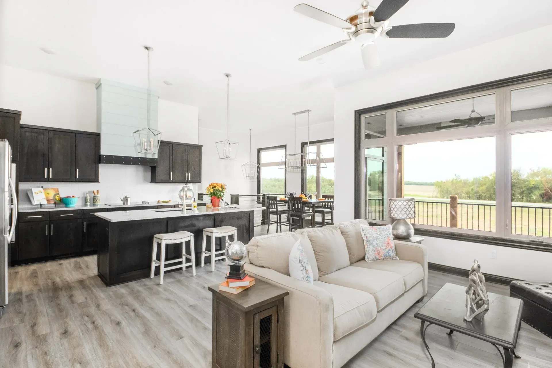 Bright modern kitchen and living room with white sofa, black cabinets, and large windows overlooking greenery