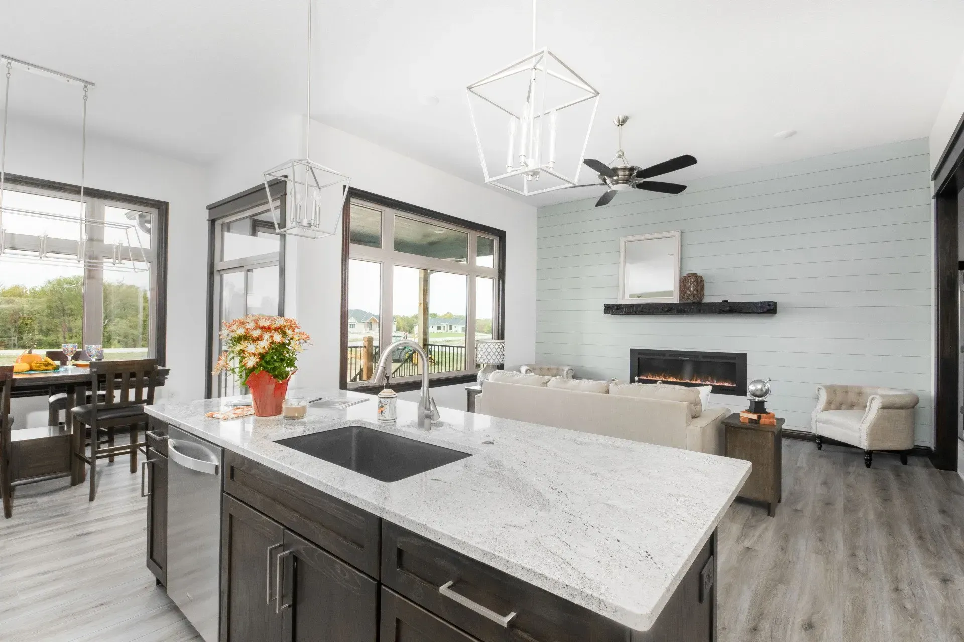 Bright modern kitchen with island, large windows, and white walls, opening to a dining area and living space