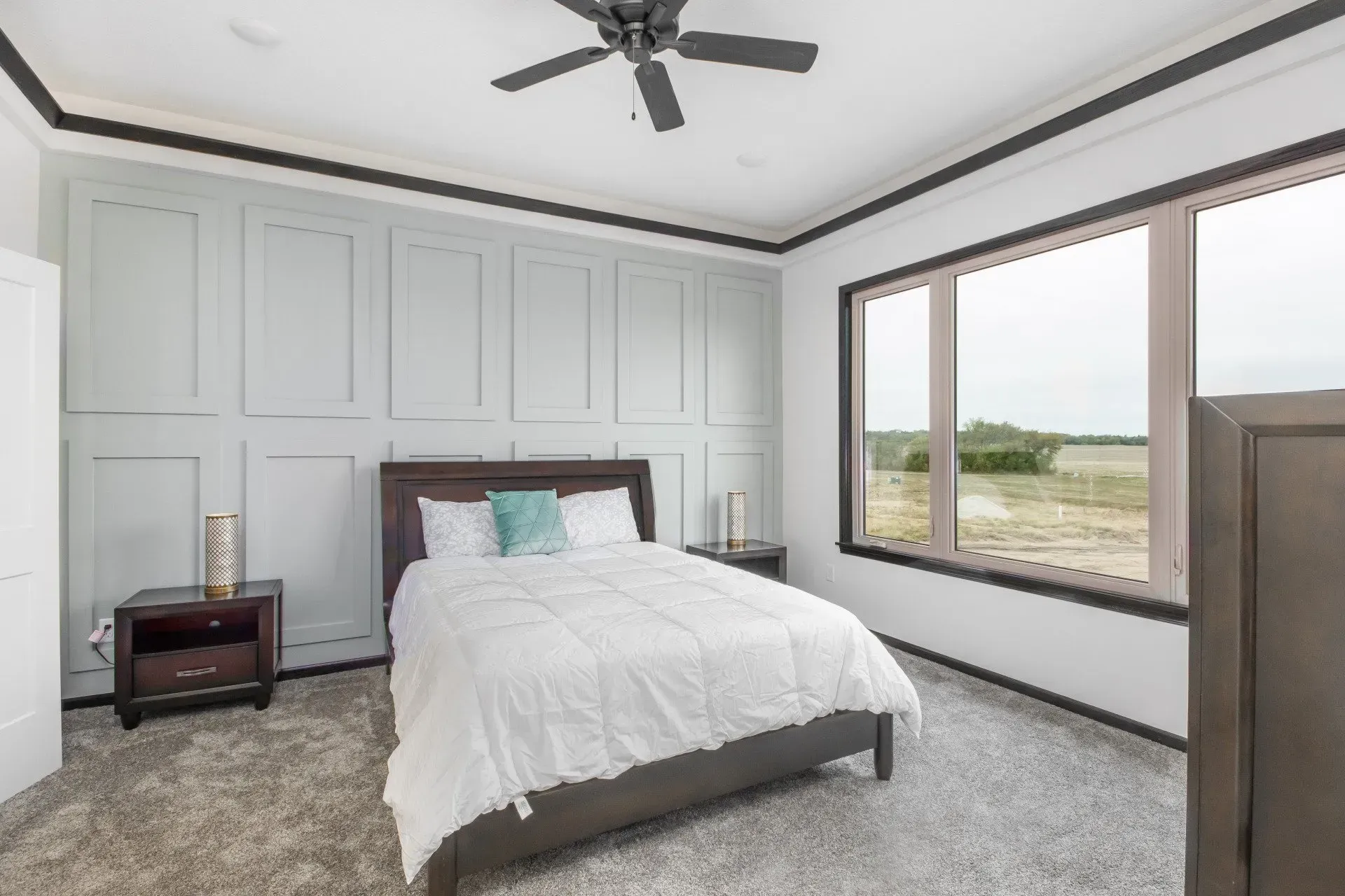 Bright bedroom with a white bed, gray walls, large windows, and a dark ceiling fan.