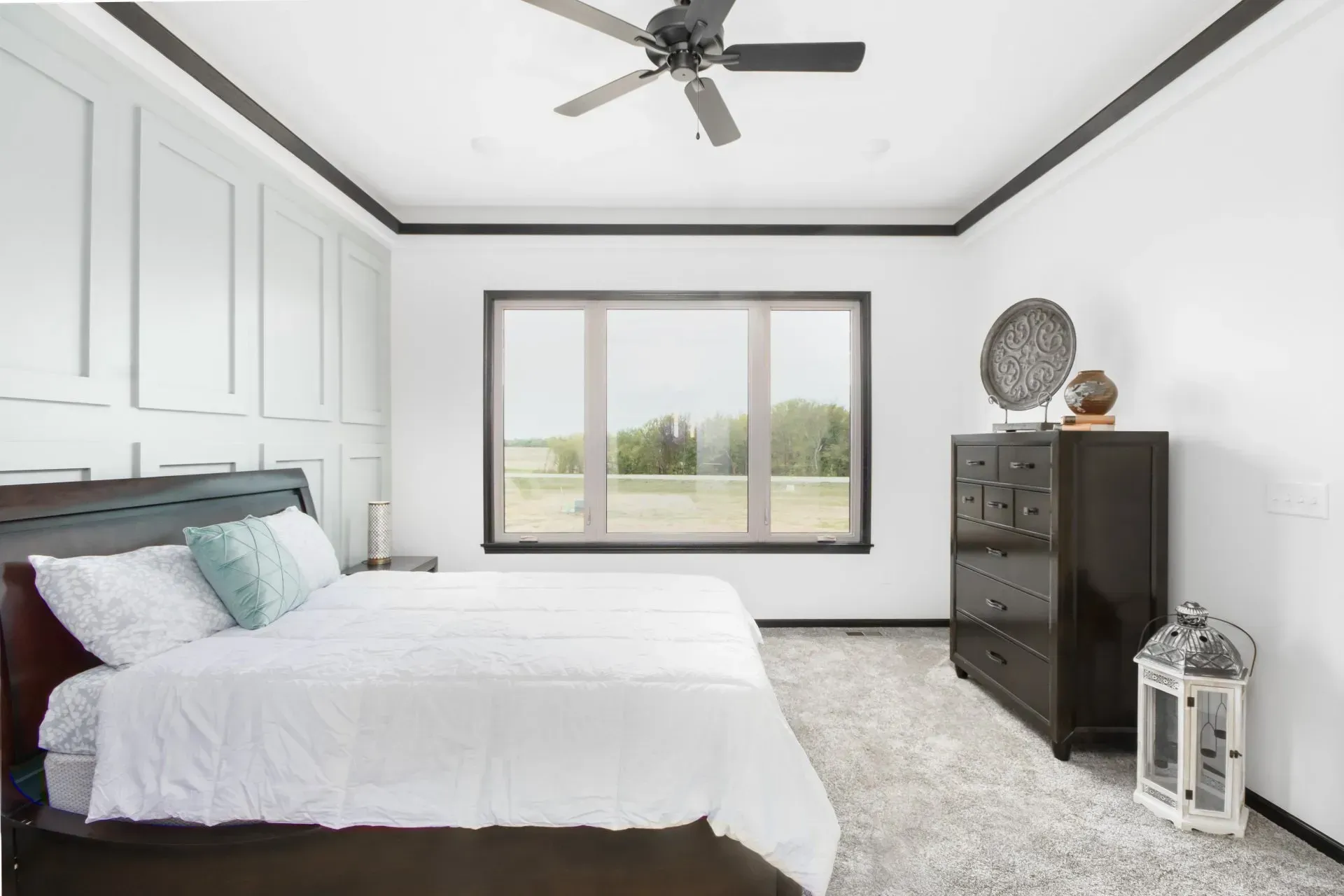 Bright bedroom with white bedding, dark wood furniture, and large window overlooking a field.