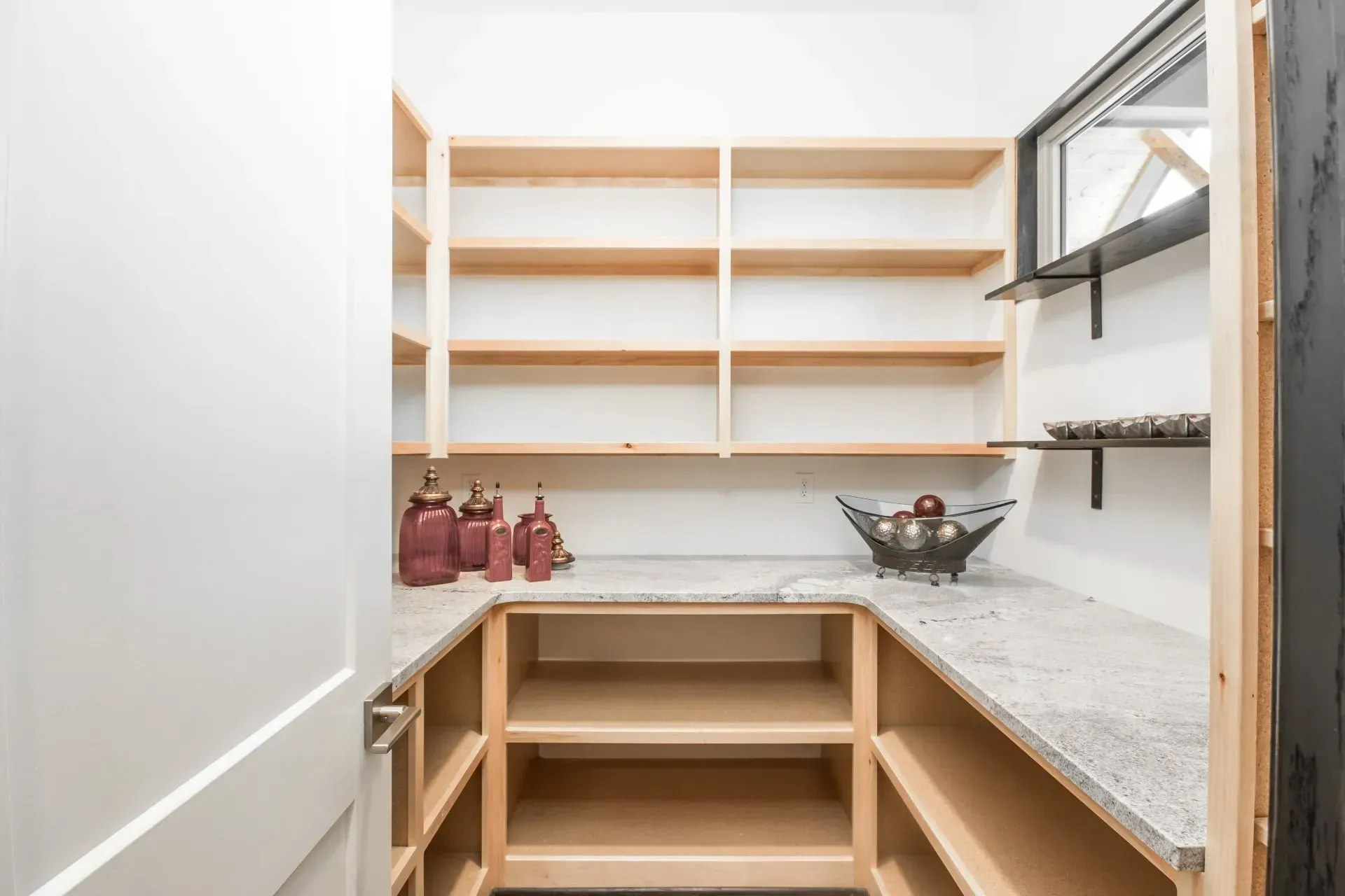 Empty walk-in pantry with white shelves, wood trim, and granite countertops on both sides