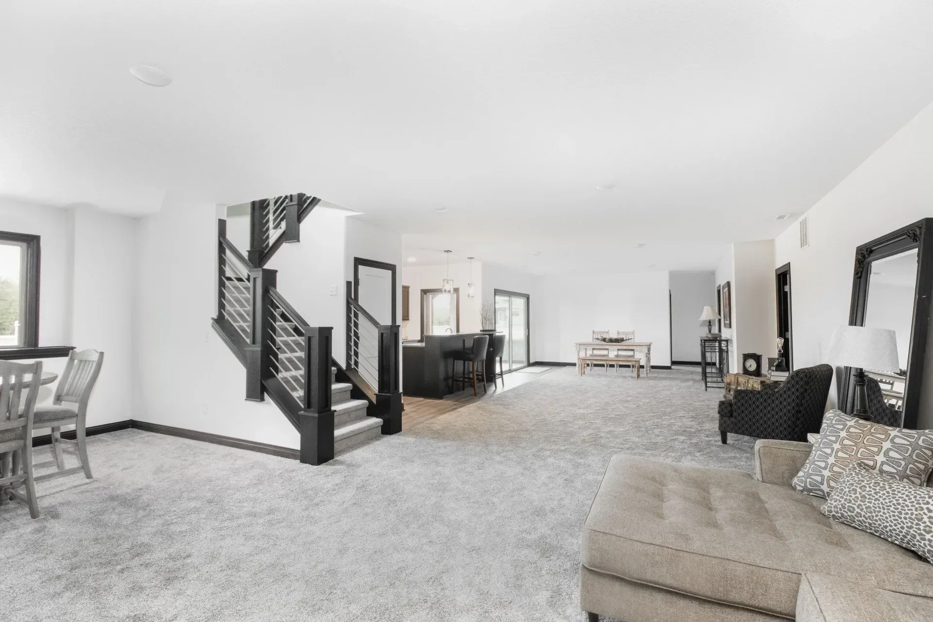 Bright open living room with gray carpet, black staircase, and beige sectional sofa near large windows.