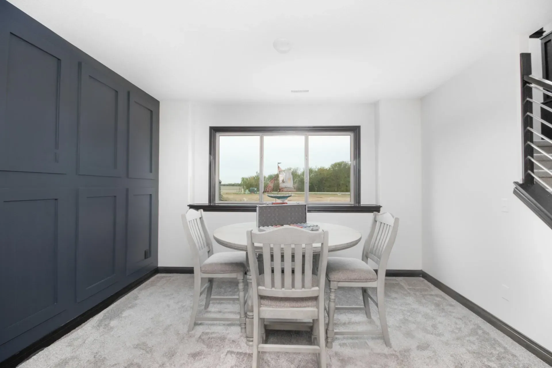 Modern dining room with a round table, white chairs, dark built-in cabinets, and a large window.