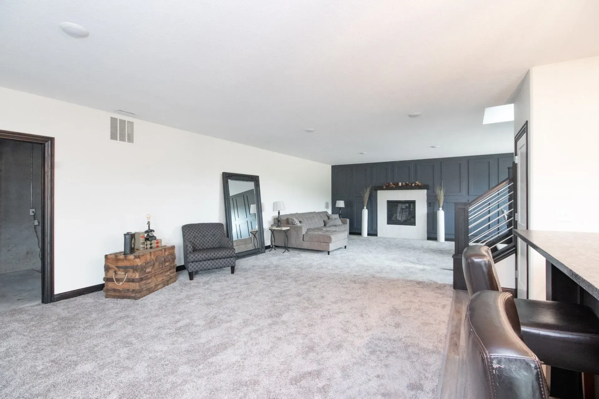 Spacious living room with gray carpet, dark accent wall, fireplace, and sparse furniture.