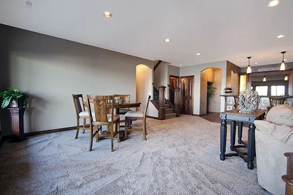 Spacious living room with carpet, wooden dining table, sectional sofa, and warm recessed lighting