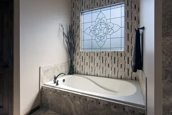 Modern bathroom with a white soaking tub, mosaic tile surround, and frosted window above it