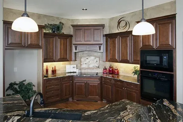 Warm kitchen with dark wood cabinets, beige countertops, pendant lights, and built-in microwave and oven.