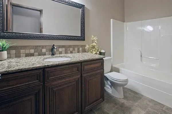 Modern bathroom with dark wood vanity, large mirror, granite countertop, toilet, and white tub shower.