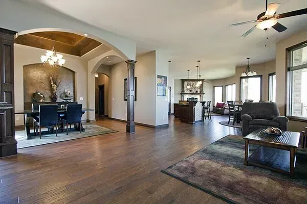 Spacious modern living room with hardwood floors, sofa, piano, and arched entryway to dining area