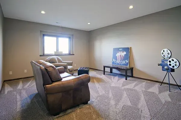 Spacious carpeted home theater with leather recliners, projector screen, and film reel decor