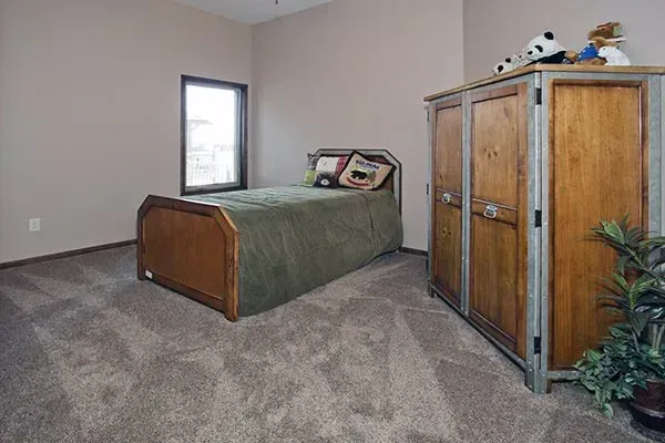 Small bedroom with a single bed, wooden wardrobe, carpeted floor, and a window.