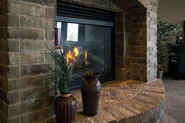Brick fireplace with a lit fire, arched stone surround, and two decorative vases on the hearth