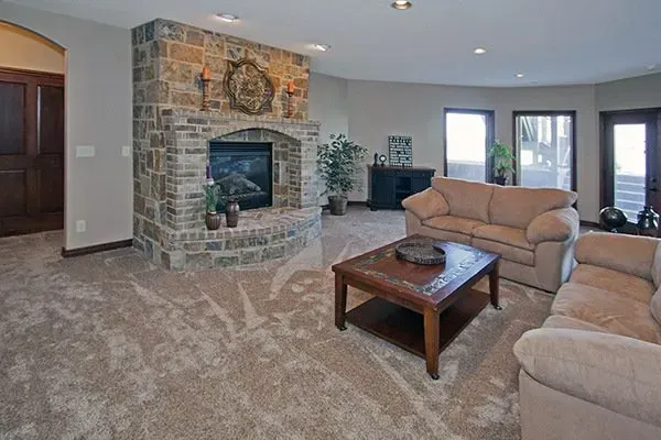 Spacious living room with stone fireplace, beige sofas, and coffee table on carpet.