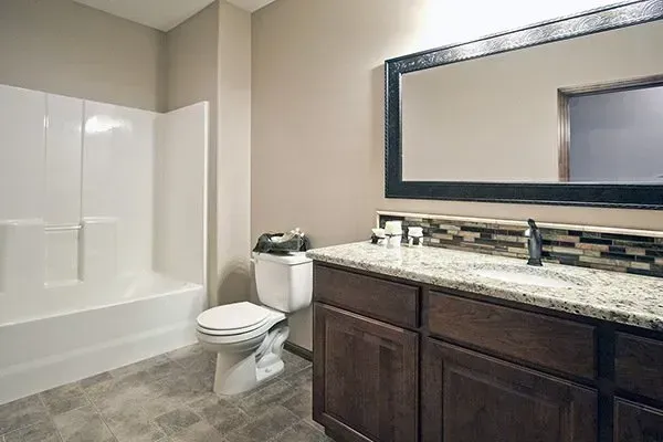 Modern bathroom with bathtub, toilet, dark wood vanity, and large mirror