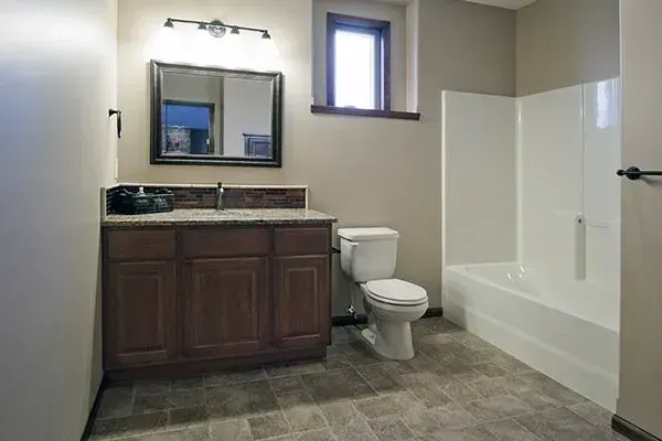 Bathroom with dark wood vanity, mirror, toilet, and white tub/shower on tiled floor.
