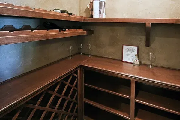 Corner of a wooden wine cellar with shelves, bottle racks, and a small sign on the counter.