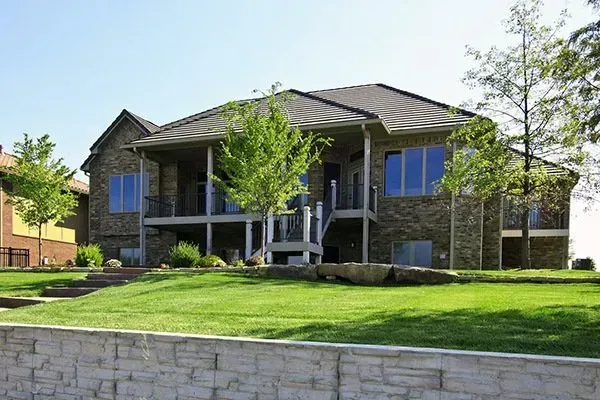 Large two-story brick house with a front lawn, white porch columns, and a stone retaining wall