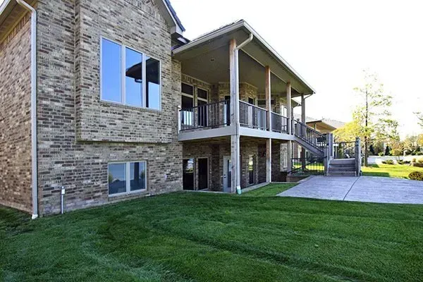 Apartment building with stone facade, covered balcony, and green lawn in bright sunlight