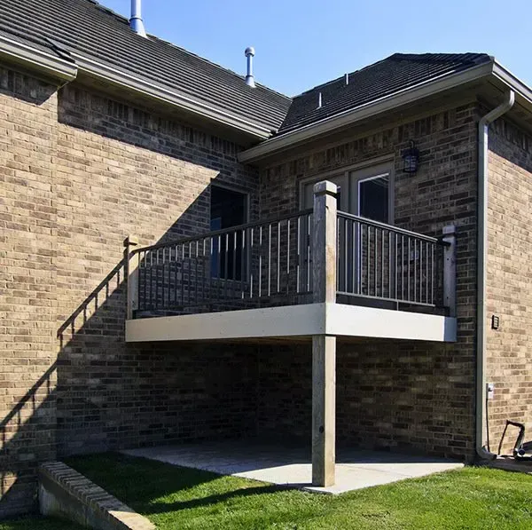 Raised balcony with black railings attached to a stone house, supported by a white column.
