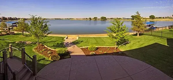 Lakefront patio and lawn with steps, landscaped garden beds, and a wide view of calm water under a clear sky