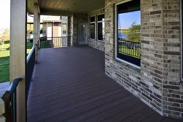 Covered brick apartment balcony with dark wood deck and railing, overlooking green space and water.