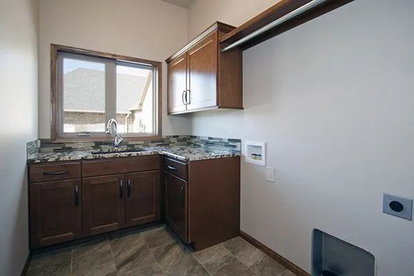 Small kitchen corner with dark wood cabinets, granite countertop, sink, and window.
