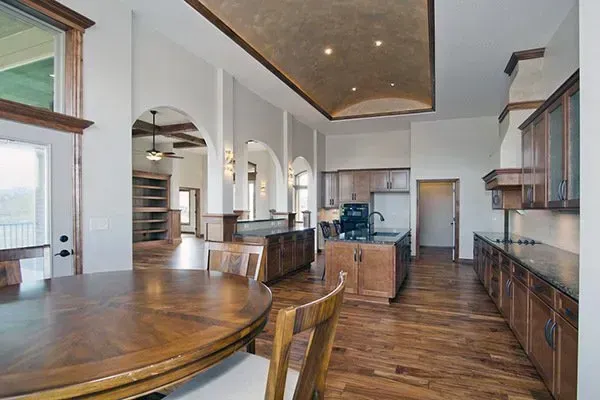 Bright modern kitchen with dark wood floors, island, cabinets, and a curved dining table overlooking large windows