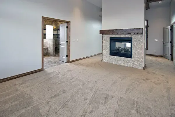 Spacious carpeted living room with stone fireplace and doorway to a kitchen area