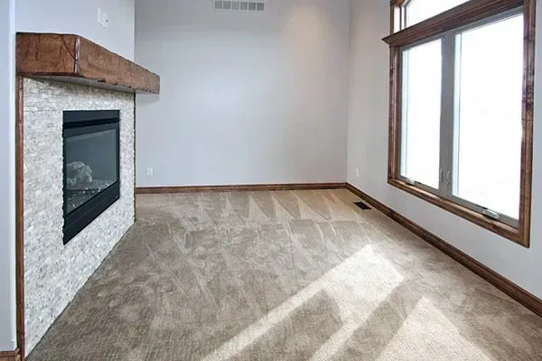 Empty living room with carpet, fireplace, and large windows letting in sunlight
