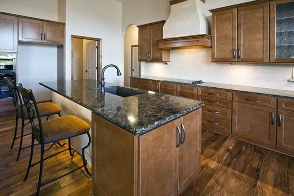 Modern kitchen with dark wood cabinets, granite island, bar stools, and stainless sink and range hood