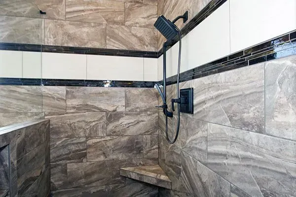 Tiled shower stall with a wall-mounted handheld showerhead and bench seat