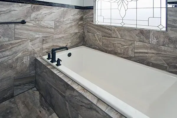 Modern bathroom with a white bathtub and gray marble tile surround