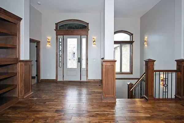 Empty hardwood-floored hallway with stairs, wooden railings, and glass-paneled front door