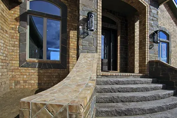 Brick house entrance with curved stone steps, windows, and a black wall lantern