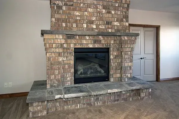 Living room with brick fireplace and mantel, stone hearth, and carpeted floor near a white door